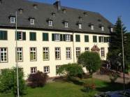 Aussenansicht der Forstschule mit Flaggenmasten und drei Personen auf der Eingangstreppe